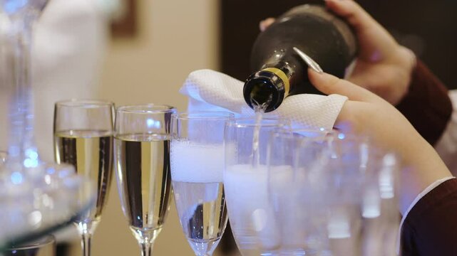 Close-up of a waiter's hands pouring champagne from a bottle into glasses. A waiter pours champagne at an event.