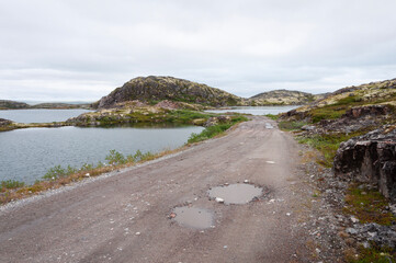Country road among rocks and lakes in tundra. Cloudy summer day. Murmansk region, Russia