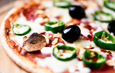 Pizza with salami and mozzarella cheese, jalapeno pepper and black olives. Wooden background. Soft focus. Close up.