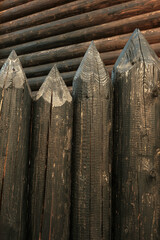 Wooden log fence against the background of the house wall.