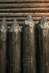 Wooden log fence against the background of the house wall.