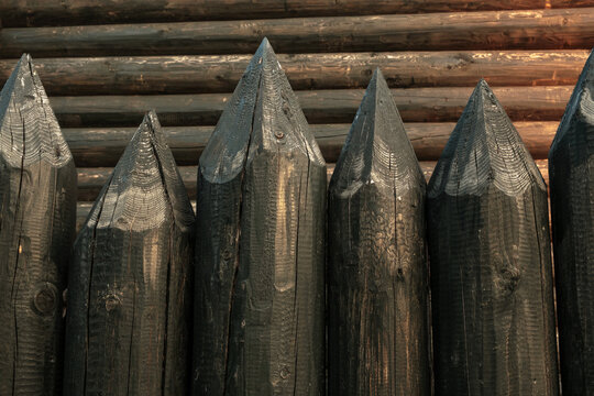 Wooden log fence against the background of the house wall.