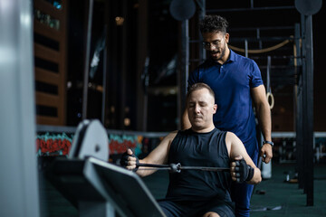 Man Doing Lat Pulldown Exercise With Trainer At Night In Gym
