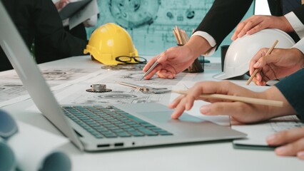 A group of engineers engages in a detailed planning session around blueprints and technical...