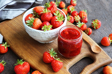 Homemade strawberry jam or marmalade in the glass jar and the fresh strawberries on the wooden rustic table .
