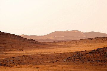 Naklejka premium Desert Landscape: A vast expanse of arid terrain stretches towards distant mountains under a hazy sky, evoking a sense of solitude and the raw beauty of the natural world.
