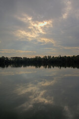 Lake with tree silhouettes reflecting in the water under a dark stormy sky in Damvallei nature reserve, Ghent, Flanders, Belgium 