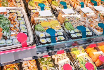 Sushi in a refrigerated display case in a sushi store, a variety of rolls, nigiri and sashimi with...