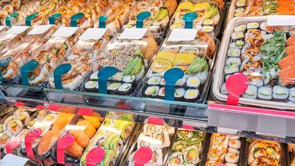 Sushi in a refrigerated display case in a sushi store, a variety of rolls, nigiri and sashimi with...