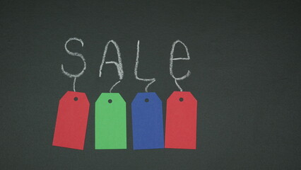 Chalk inscription SALE on a school blackboard with colored shopping tags under the letters