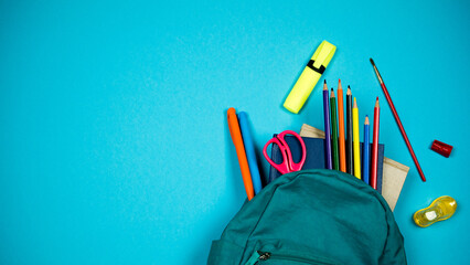School backpack with colored school supplies sticking out of it on blue background. Back to school concept