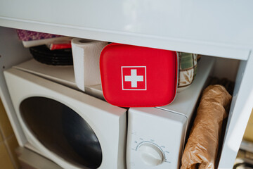 A red First Aid Kit positioned conveniently on top of the washing machine, easily accessible for home storage in case of any emergency health situations that may arise