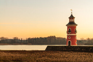 Pink lighthouse near Moritzburg Castle bathed in gentle light sunset. Lighthouse contrasts beautifully with multi-colored sky against picturesque landscape. Architecture Germany