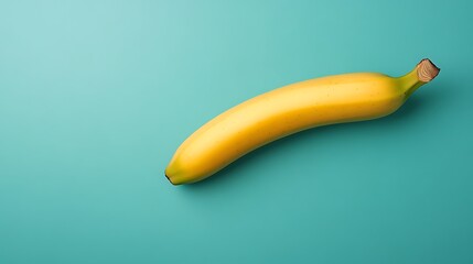 Single ripe banana lies on plain teal background, top-down, for healthy eating concepts