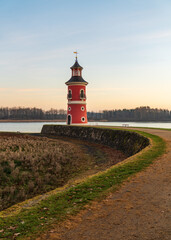 Lighthouse on lake near Moritzburg at sunset, with warm glow sky reflecting on water. Silhouette castle in background adds charm serene German landscape