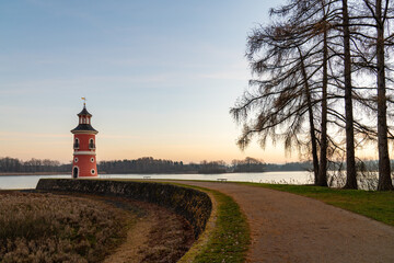 Lighthouse on lake near Moritzburg at sunset, with warm glow sky reflecting on water. Silhouette...