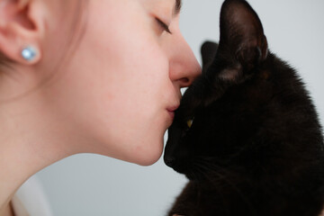Happy young beautiful caucasian woman kissing and holding a black cat. Playing with pet at home. Love, coziness, leisure, animal protection concept. 