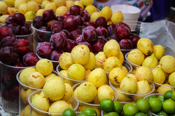 Fresh guavas, plums, and limes in clear cups at a market