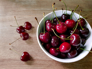 Ripe red cherries in white cup placed on wooden table top. Top view of sweet fruit with natural light.