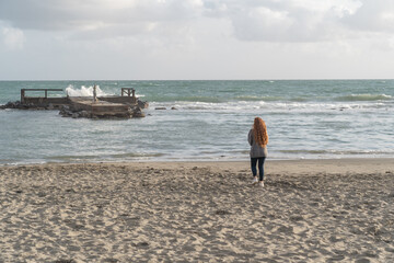 Woman walking on the beach watching the wild sea.
