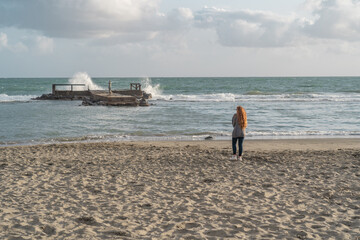 Woman walking on the beach watching the wild sea.
