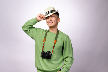 An Asian man in a green sweater is smiling while tipping his fedora hat. He has a camera hanging around his neck, giving off a traveler or photographer vibe against a white background