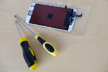 Smartphone repair process with screwdriver and disassembled mobile phone on wooden table. Tech...