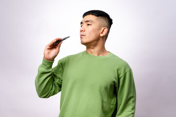 An Asian man wearing a green sweatshirt is vaping, exhaling a visible cloud of vapor with his eyes...