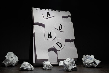 oświetlony otwarty brulion z napisem ADHD z powyrywanych bez ładu kawałków papieru, na ciemnym tle