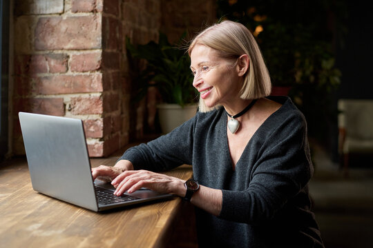 Elderly Woman Smiling While Using Laptop at a Cafe
