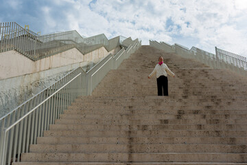 A woman stands at the top of a large outdoor staircase, arms open, embracing the sky. The stairs...