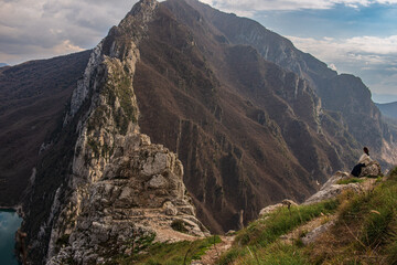 A traveler stands on a grassy ridge, staring into the vast mountain range ahead, where cliffs and valleys create a mesmerizing landscape of contrast and natural beauty.