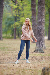 Obraz premium Attractive blue eyed blonde woman walk on the city park. Girl wear beige hoodie, pink bag and look happy and smiles.