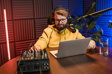Cheerful young man recording podcast in studio. Confident man with headphones and microphone...