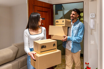 Happy couple carrying cardboard boxes entering new home