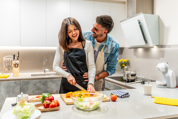 Happy couple preparing vegetable salad in modern kitchen