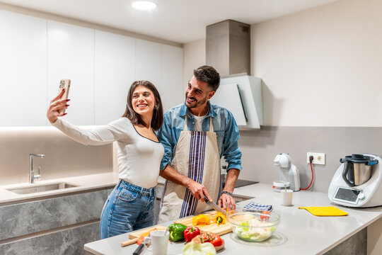 Happy couple taking selfie while preparing healthy meal in modern kitchen
