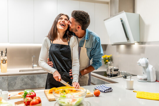 Happy couple preparing dinner together, embracing and smiling in modern kitchen - Powered by Adobe