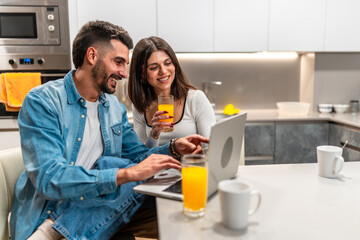 Couple using laptop and drinking orange juice in kitchen