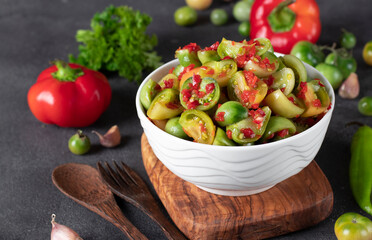 Salad of green tomatoes with hot peppers and garlic in white salad bowl