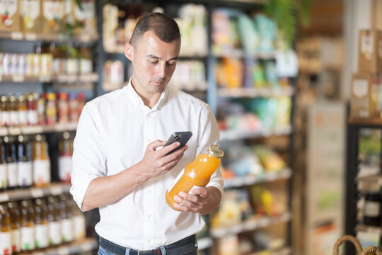 Man in supermarket scan QR code bottle of drink. Male buyer photo information on packaging of bio product.