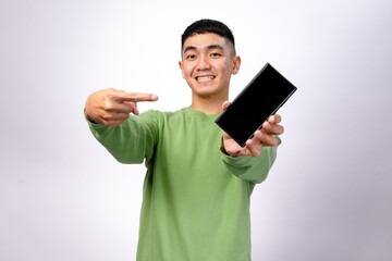 An Asian man in a green sweatshirt is smiling and pointing at a smartphone with a blank screen. He holds the phone in one hand while gesturing towards it with excitement. The background is white