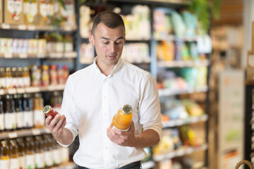 Man in bio supermarket buys drink. Male buyer examines packaging bottle of product and reads information on label