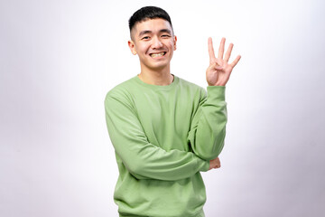 An Asian man in a green sweatshirt is smiling while holding up four fingers on his right hand. His...