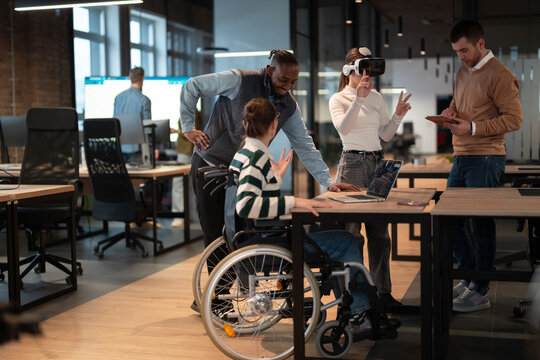 Disabled businesswoman in a wheelchair working in modern coworking office. Team around is using virtual reality goggles, collaborating with the latest technology in an open space startup creative