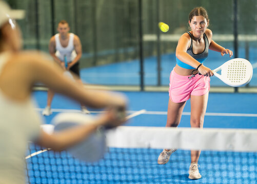 Young girl paired with a man plays padel on an indoor tennis court