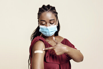 Black lady in protective face mask pointing at plaster on her arm, got vaccinated against...