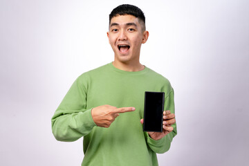 An Asian man in a green sweatshirt is smiling and pointing at a smartphone with a blank screen. He holds the phone in one hand while gesturing towards it with excitement. The background is white