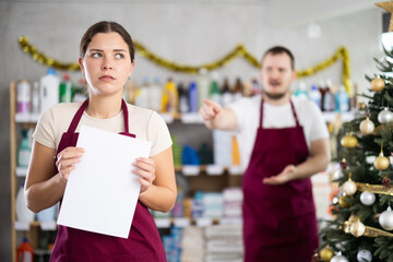Angry salesman scolding at female assistant in small hardware store decorated for New Year...