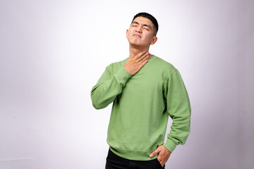 An Asian man in a green sweatshirt touches his throat with one hand, his face showing discomfort...